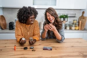 Two cheerful multi-ethnic female friends are preparing a joint of legal marijuana in a domestic kitchen
