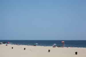 Diverse group of people relax by the beach on a summers day. Group of young black kids, hipsters of all ethnicity, young and old chill by the sea. Life guard on duty. Colorful parasols dot the beach.