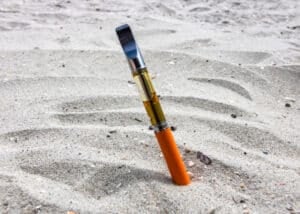 Electric vape pen full of THC oil resting in the sand.